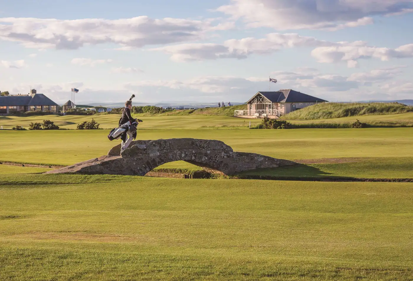 Golfer walking across a stone bridge on a scenic golf course